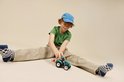 Jongen met rood haar, blauwe pet, groen T-shirt, beige broek, en blauw-witte geruite sokken, speelt met een turquoise tractor.