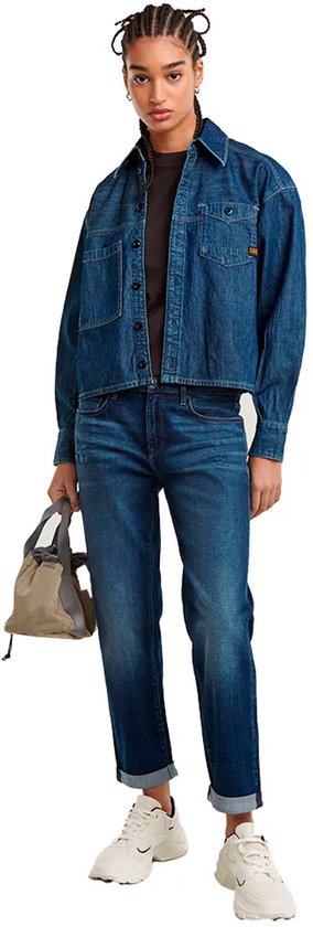 Model draagt een donkerblauwe jeans met omgeslagen broekspijpen en een denim jasje.