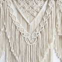 Gedetailleerde close-up van een crèmekleurig macramé wandkleed met complexe knoop- en franjepatronen.