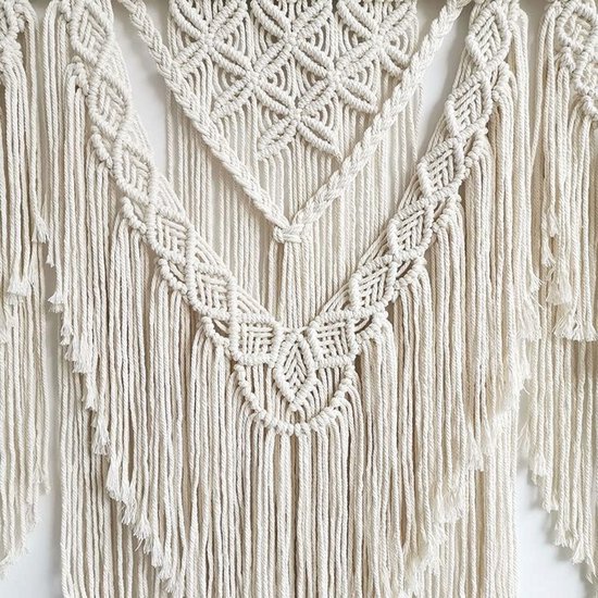 Gedetailleerde close-up van een crèmekleurig macramé wandkleed met complexe knoop- en franjepatronen.