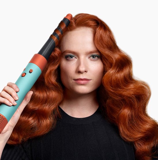 Vrouw met rood, golvend haar houdt Dyson Airwrap i.d. (blauw/oranje) vast.