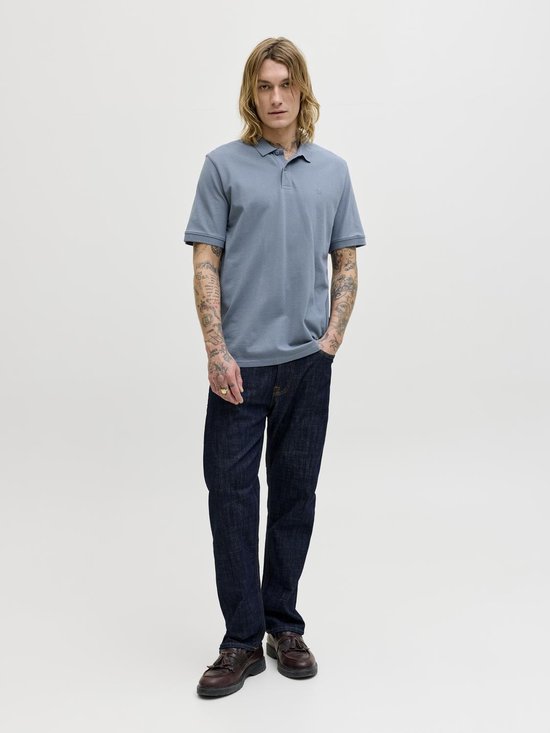 Blauwe polo met korte mouwen, gedragen door een model met tatoeages. De polo heeft een kraag en twee knoopjes bij de hals.