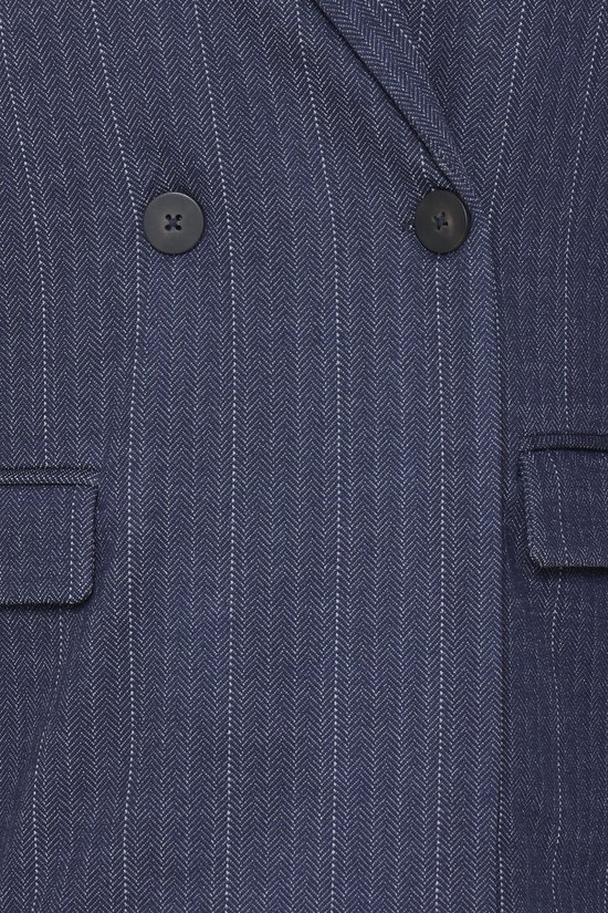 Close-up van de donkerblauwe blazer met krijtstrepen, twee zwarte knopen en klepzakken.