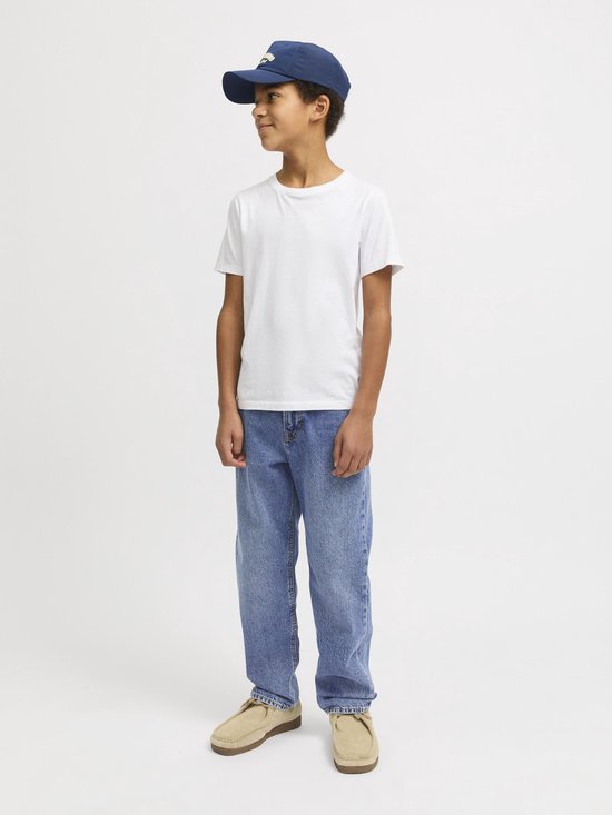 Jongen zittend, kijkend naar links, in een lichtblauwe spijkerbroek, wit T-shirt en donkerblauwe pet.