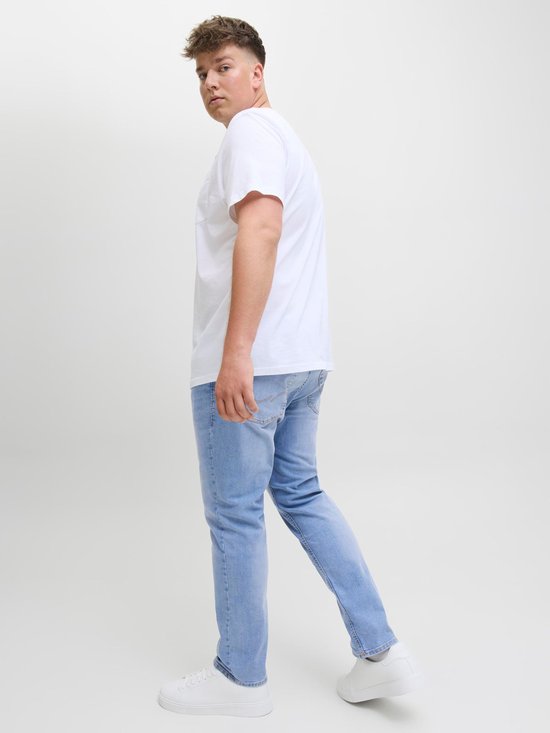 Man draagt een witte T-shirt met opgestoken zak en een lichtblauwe spijkerbroek, van de zijkant gezien.