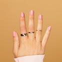 Hand met roze gelakte nagels, met drie ringen: een brede zilverkleurige ring, een slanke gouden ring en een zeer dunne gouden ring.