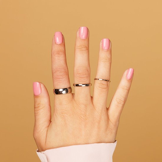 Hand met roze gelakte nagels, met drie ringen: een brede zilverkleurige ring, een slanke gouden ring en een zeer dunne gouden ring.