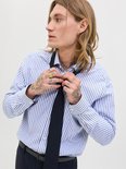 Man met lang blond haar, tatoeages, draagt een blauw-wit gestreept overhemd en knoopt een zwarte stropdas vast.