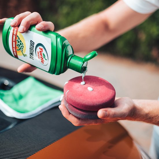 Handen knijpen in groene Turtle Wax fles boven rode applicator met witte wax druppels.