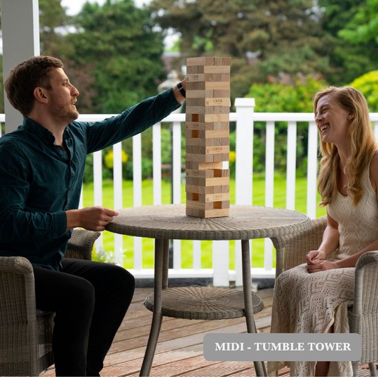 Man en vrouw spelen stapeltoren spel aan ronde tafel op een terras. Houten toren en 'UBER GAMES' logo's.