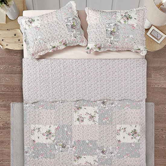 Bovenaanzicht van een bed met een patchwork sprei. Patronen van roze bloemen, groen, roze en tekst op de sprei en kussens.