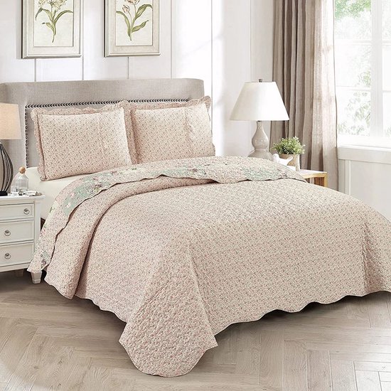 Een bed met een sprei en kussens met een fijn roze bloemenpatroon. De sprei heeft een golvende rand.