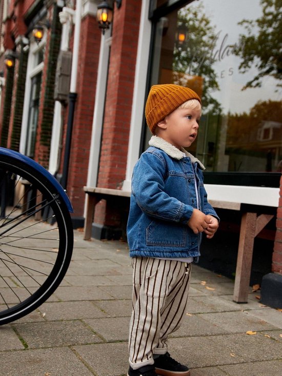 Jongen met blond haar in een blauw denim spijkerjack met borgkraag, staand buiten.