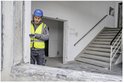 Bouwvakker met blauwe helm en geel hesje kijkt op laser afstandsmeter bij trap.