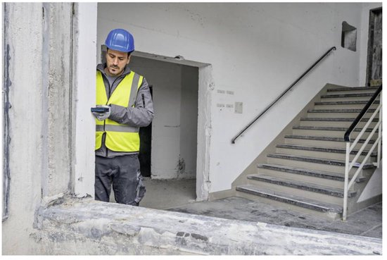 Bouwvakker met blauwe helm en geel hesje kijkt op laser afstandsmeter bij trap.
