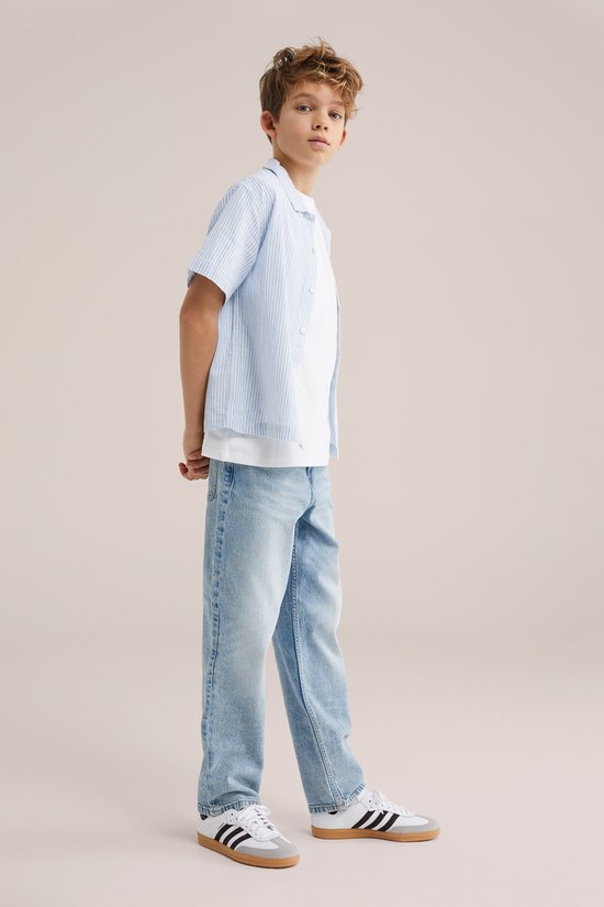 Jongen in een lichtblauwe gestreepte korte mouw overhemd en lichte jeans.