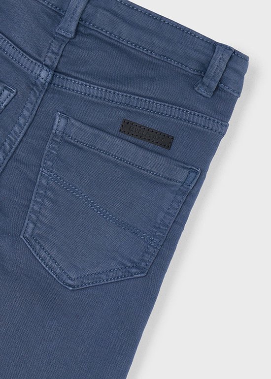 Detail van de achterkant van een effen blauwe jongensbroek met logo patch.
