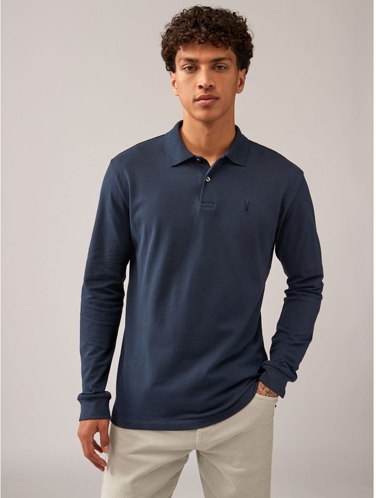 Man in donkerblauwe polo met lange mouwen en geborduurd logo, beige broek.