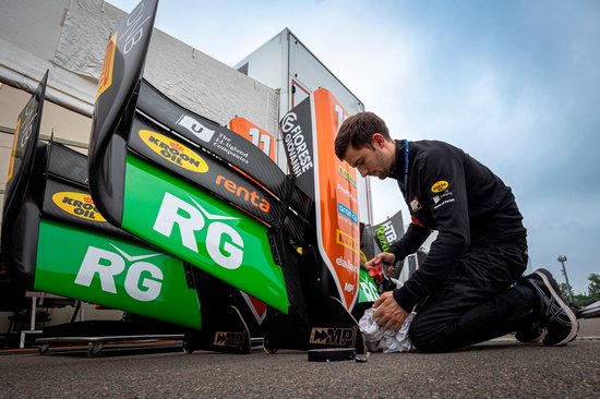 Een monteur met een overall werkt aan de grote groene en zwarte achtervleugels van een racewagen.
