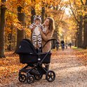 Vrouw houdt baby in zebra onesie vast bij een kinderwagen in het bos.
