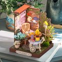 Miniatuur theeservies in een tuin met roze deur, bakstenen muur en bloemen. Afmetingen 11.5x10x11cm.
