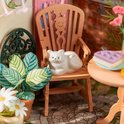 Witte kat op een houten stoel naast een plant met gestreepte bladeren.