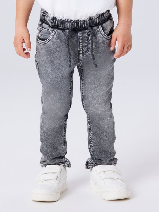 Onderlichaam van een jongetje in een grijze jeans, gedetailleerd met strikceintuur en witte sneakers.