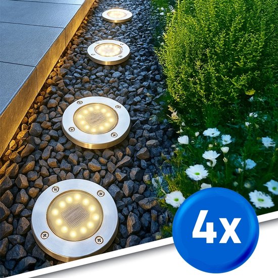 Vier zilverkleurige, ronde grondspots met zonnepanelen en 12 LED's, geplaatst in grind naast een struik en bloemen.