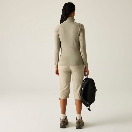 Model draagt beige fleece jas, beige capri broek en wandelschoenen, kijkt weg.