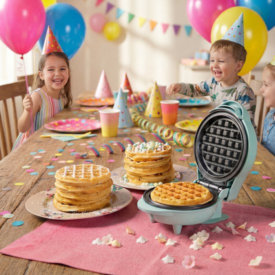 Blauw mini wafelijzer op kinderverjaardag. Twee stapels wafels met versiering, en een wafel in het ijzer. Kinderen met feestmutsen op de achtergrond.