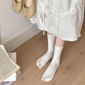 Witte tabi sokken met ribbelpatroon en een split tussen de grote teen en de andere tenen, gedragen met een witte jurk.