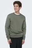 Een man met krullend haar draagt een mosgroene sweater met ronde hals en zwarte broek.