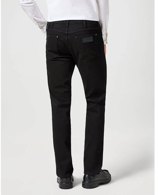 Man in zwarte jeans en wit overhemd, staand, achterkant zichtbaar.