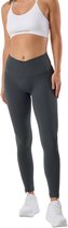 Model in donkergrijze legging met gekruiste hoge taille, witte sportbeha en witte sneakers.