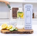 Glazen fles met citroen en komkommer, naast een glas en een doos.