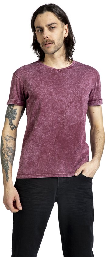 Een man met lang donker haar, in een bordeauxrode, verweerde T-shirt met opgerolde mouwen en zwarte jeans.