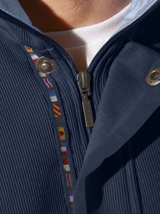 Close-up van de rits van een donkerblauwe trui met aan de binnenzijde een band met nautische vlaggetjes.