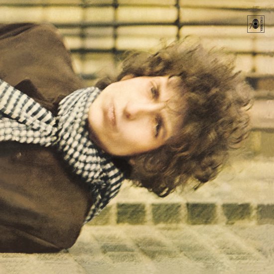 Bob Dylan, leunend, met warrig bruin haar en een zwart-wit geblokt sjaaltje.