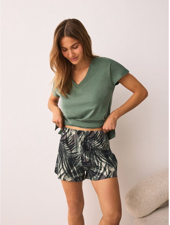 Vrouw in een groen V-hals T-shirt en een short met bladerenprint, staand.