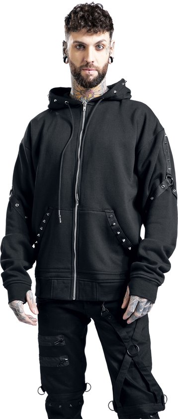 Man met tatoeages, baard en piercings draagt een zwarte rits hoodie met studs en banden aan de mouwen en broek.