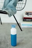 Blauwe Dopper drinkfles met witte bovenkant en blauwe dop, op een grijze vloer.