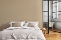Slaapkamer met beige muur, een bed met wit en grijs beddengoed, en een badkuip zichtbaar door een glazen deur.