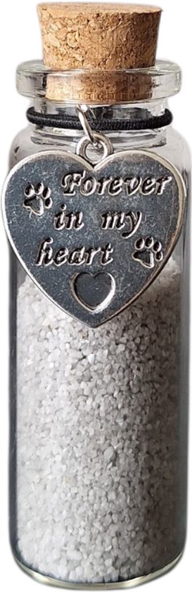 Glazen flesje met kurk, gevuld met lichtgrijs zand en een zilveren hartvormige bedel met 'Forever in my heart' en pootafdrukken.