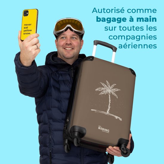 Man met skibril en muts neemt selfie met gele telefoon, houdt bruine koffer met palmboom op.