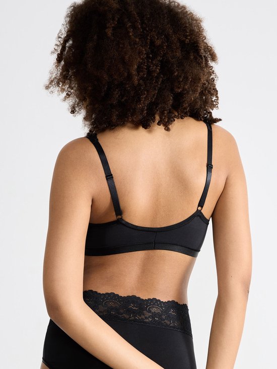 Model met krullend haar, rug zichtbaar, draagt een zwarte bralette en slip met kanten randen.