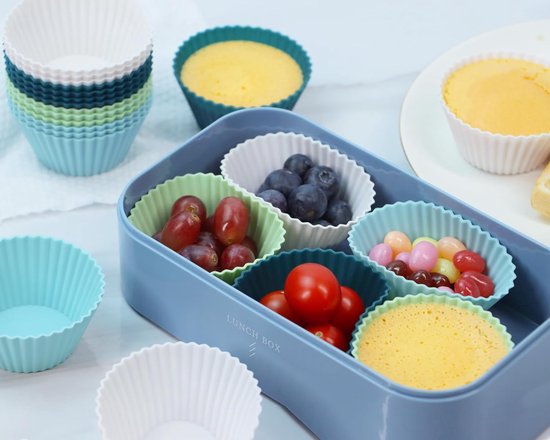 Een blauwe lunchbox met zes siliconen vormpjes gevuld met druiven, bosbessen, snoepjes, cherrytomaatjes en cake.