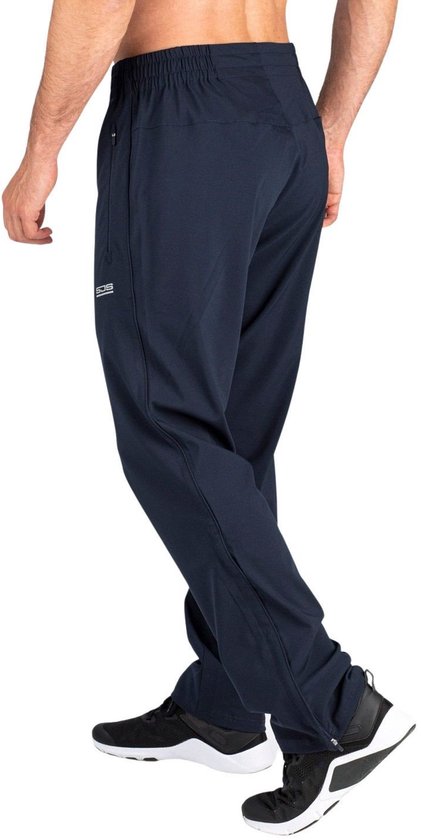 Man in donkerblauwe sportbroek met ritsen aan de zijkant en witte sneakers.
