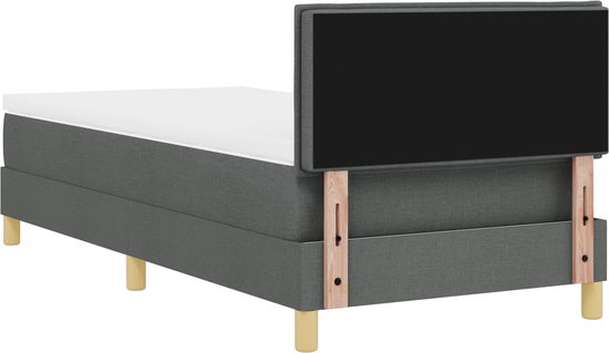 Donkergrijze boxspring met zwart hoofdbord, witte matras en houten poten.