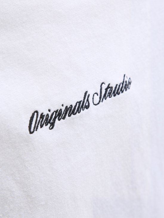 Close-up van de zwarte "Originals Studio" tekst geborduurd op een wit T-shirt.