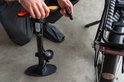 Persoon met horloge gebruikt zwarte fietspomp met oranje handvat en drukmeter naast een fietswiel.